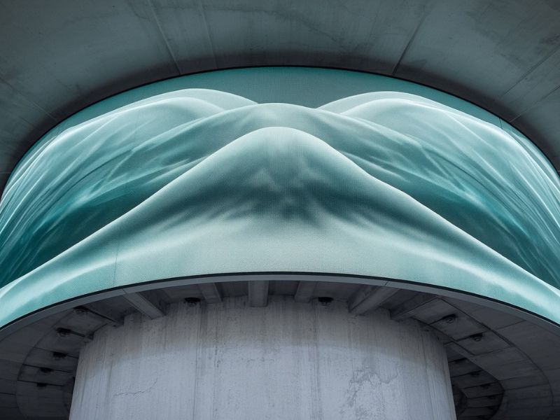 Large curved outdoor LED display integrated into a modern building façade showcasing fluid digital visuals on an architectural structure - ALEDA Large curved outdoor LED display integrated into a modern building façade showcasing fluid digital visuals on an architectural structure